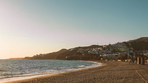 Free Scenic view of a beach and mountains at sunset, featuring calm ocean waves and a tranquil coastline. Stock Photo