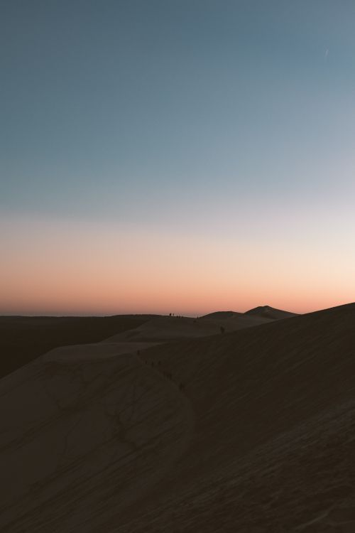 Free Serene desert view at dusk with gently sloping sand dunes against a colorful sky. Stock Photo