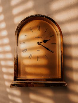 Close-up of a classic brass wall clock with Roman numerals in warm lighting.