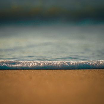 Close-up of seafoam over golden sand, capturing the peaceful ocean scene in Riohacha, Colombia.