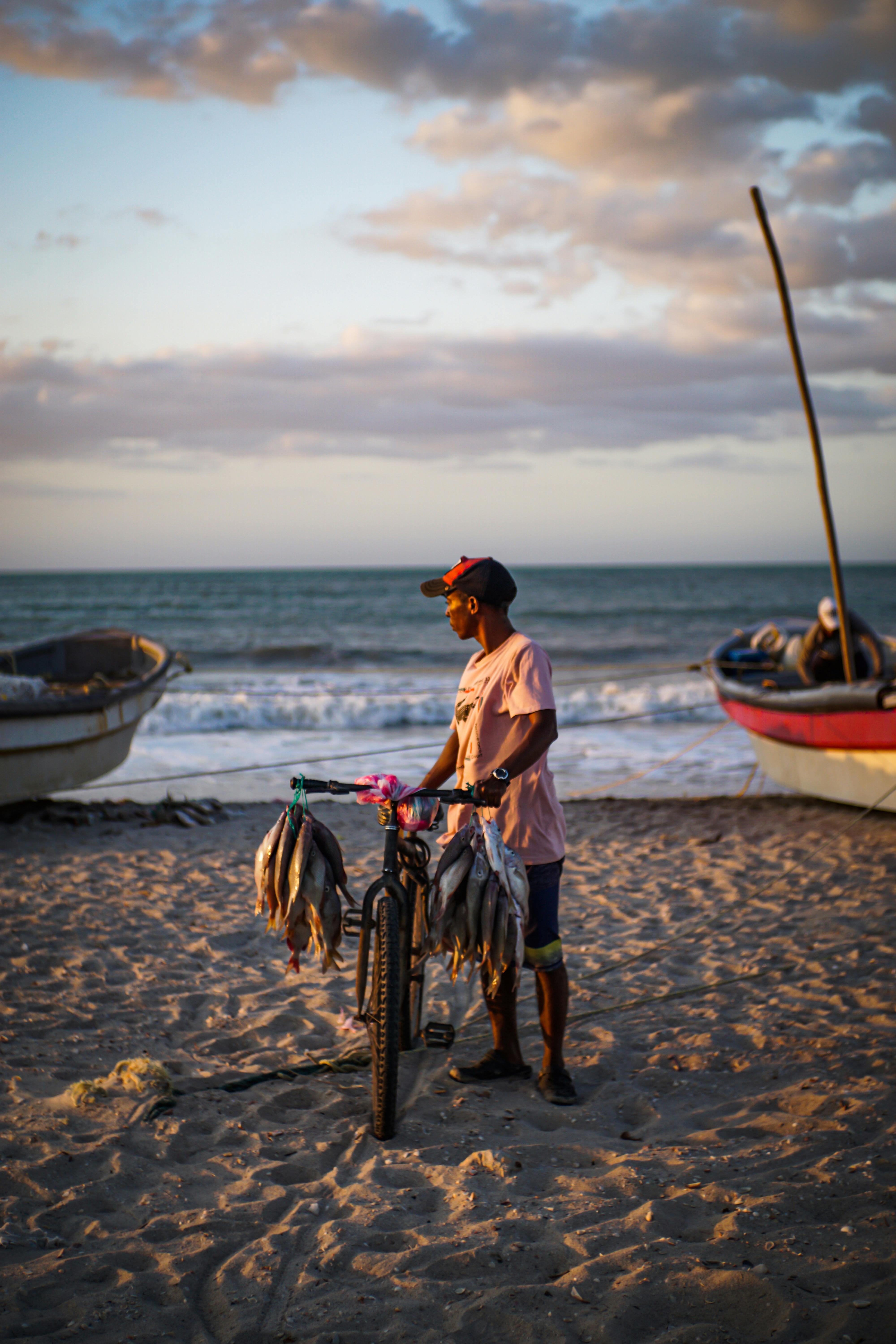 A fisherman on Riohacha beach in Colombia displays fresh fish on his bicycle during a vibrant sunset.