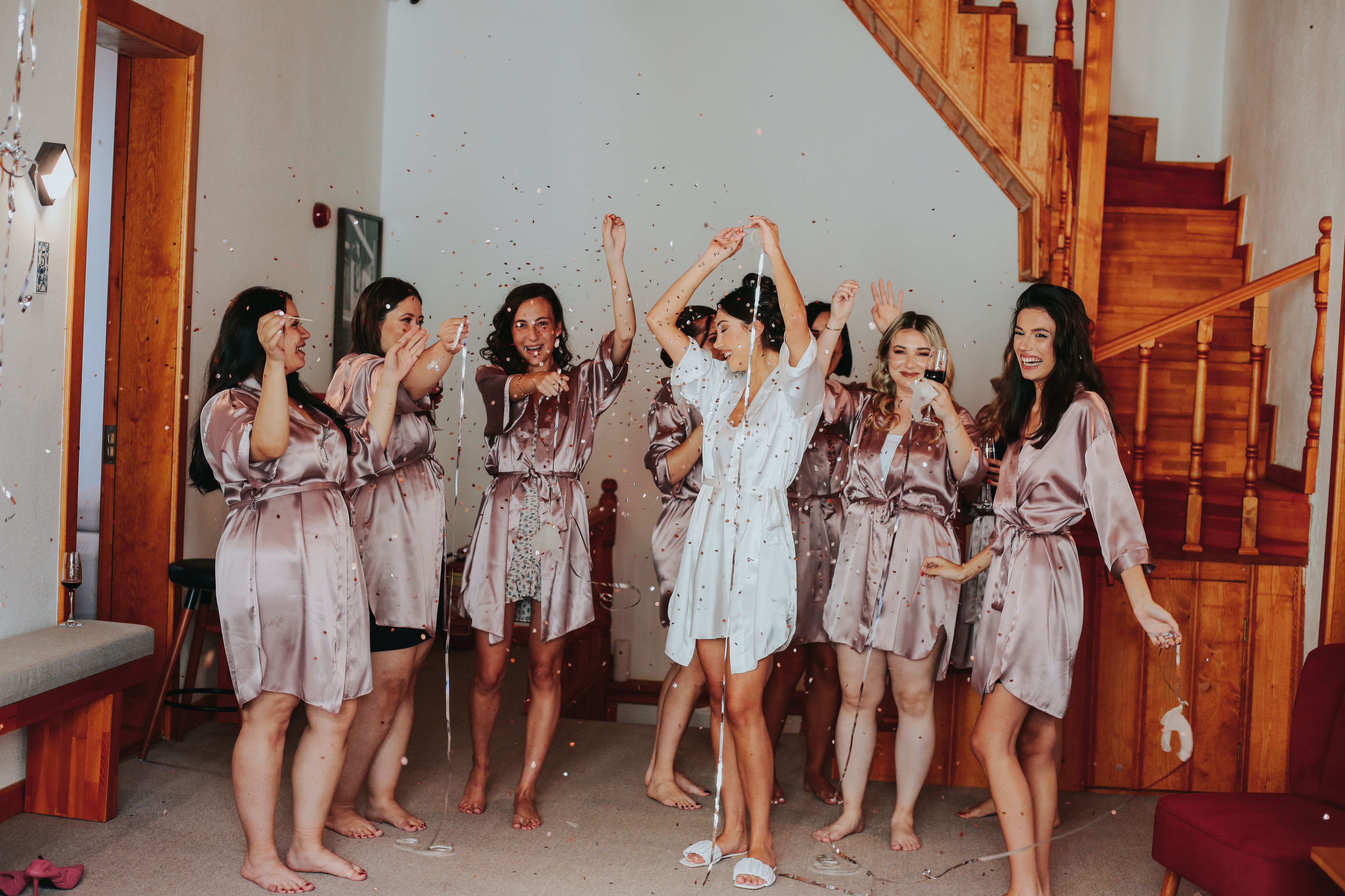 A group of women in bathrobes celebrating inside with confetti and laughter.