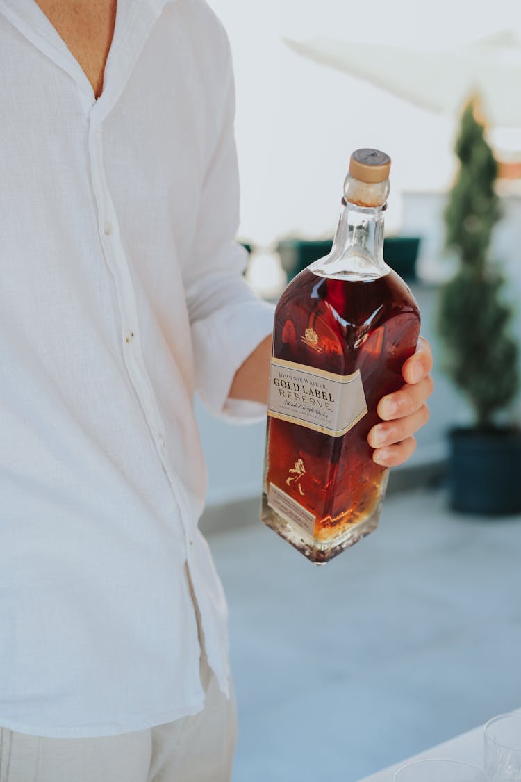 A Person's Hand Holding A Bottle Of Whiskey