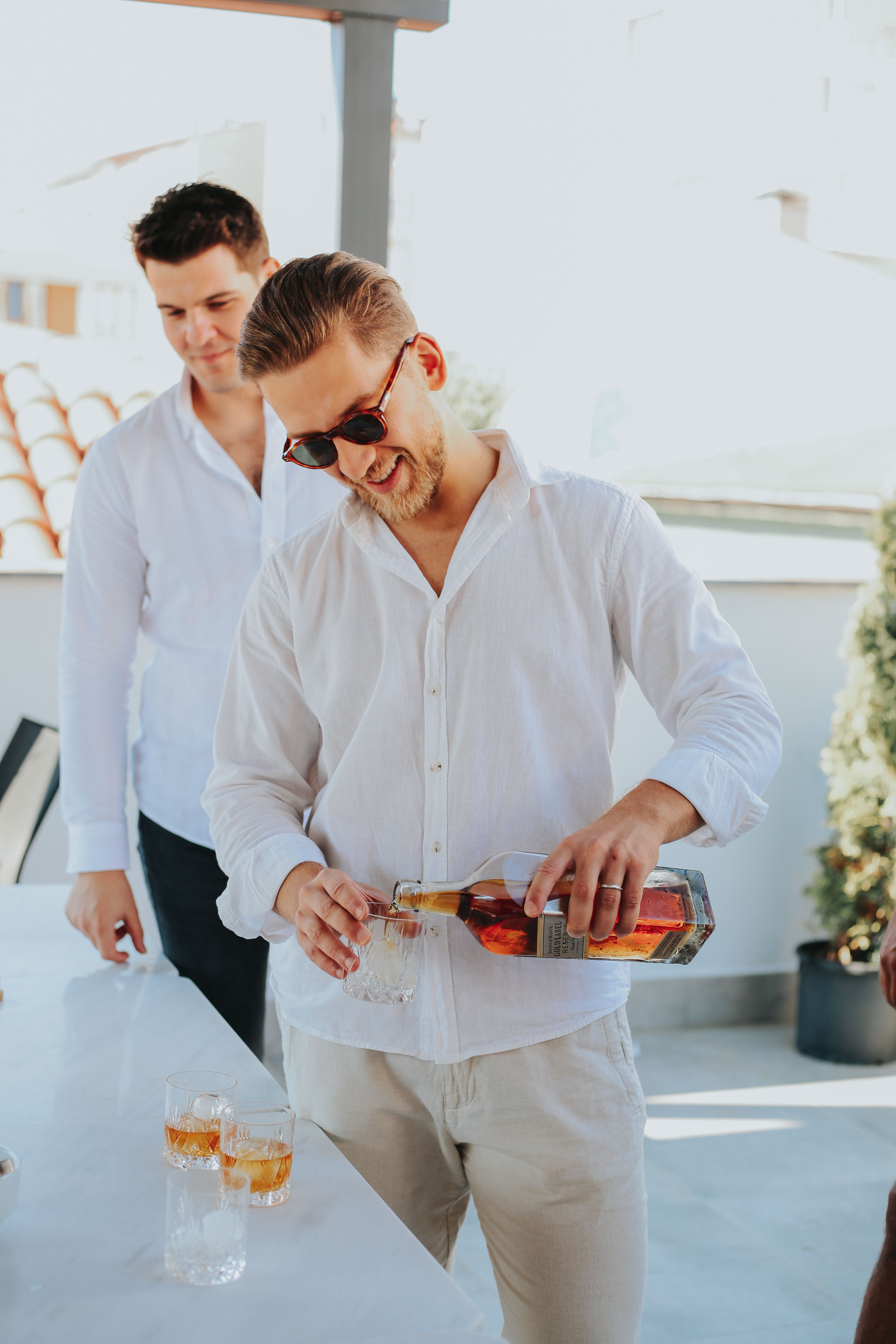Men pouring and enjoying whiskey outside in a casual social gathering.
