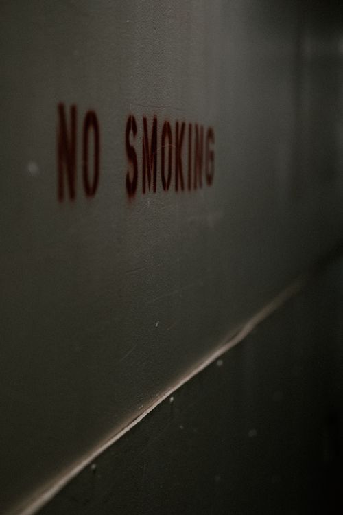 Free Moody 'No Smoking' sign on a dimly lit wall, emphasizing prohibition. Stock Photo