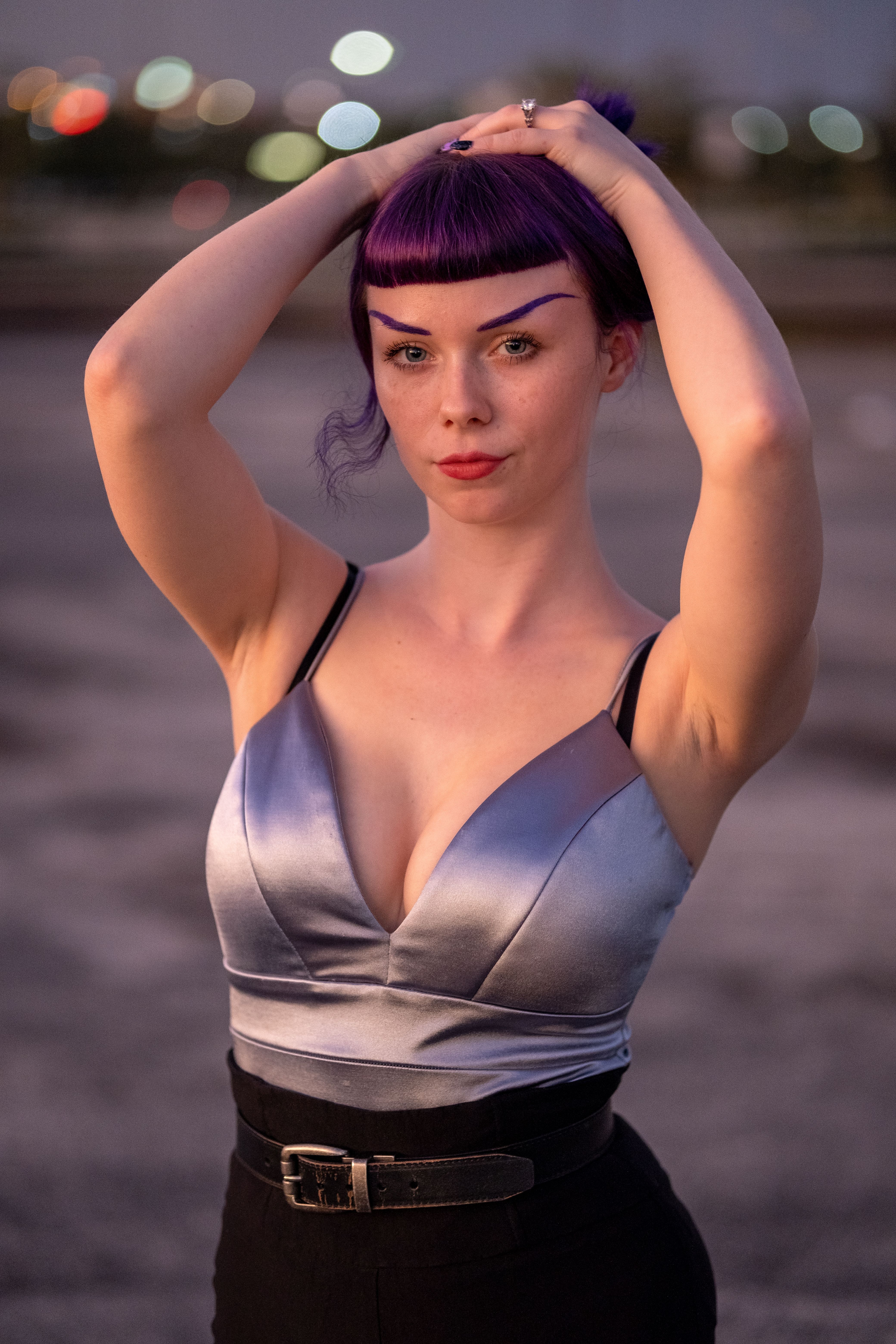 Portrait of a woman with purple hair in a fashionable outfit posing confidently at sunset outdoors.