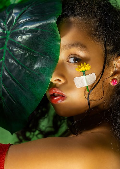 Free Creative portrait of a woman with a leaf backdrop and flower decoration on her face. Stock Photo