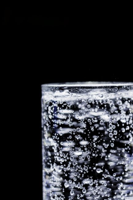 Two clear glasses of carbonated water side by side, one labeled club soda showing a slight cloudiness from added minerals, the other sparkling water with visible fine bubbles rising.