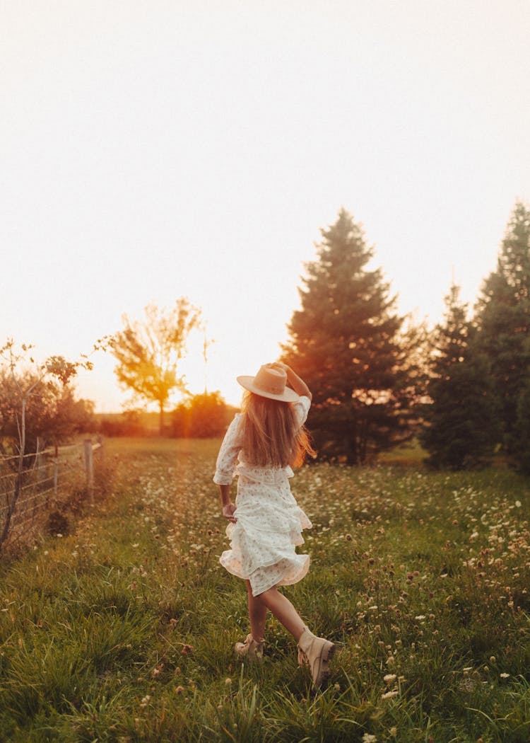 A Woman In White Dress Running On Green Grass Field