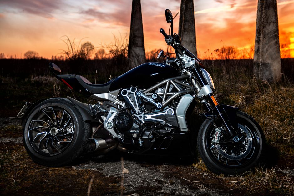 Side view of a Ducati motorcycle parked outdoors against a stunning sunset backdrop.