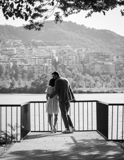 Grayscale Photo of Couple Standing near Railing