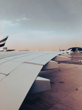 View of an airplane wing at Dubai Airport during sunset, capturing the serene ambiance and modern travel vibe.