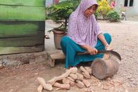 A Muslim woman in a hijab skillfully cutting wood with a machete outdoors.