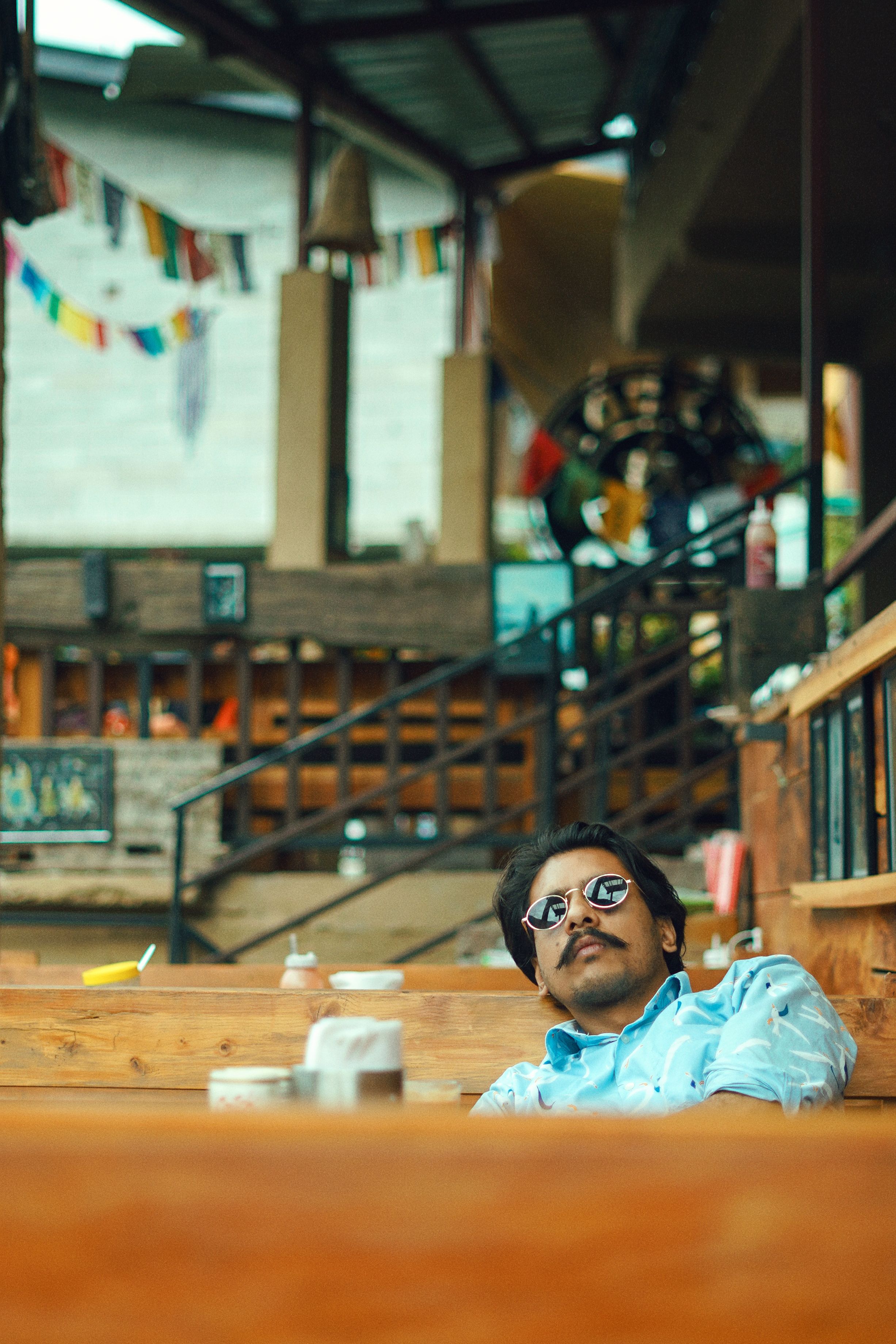 Man in sunglasses sitting relaxed in an Indian restaurant, showcasing casual vibes.