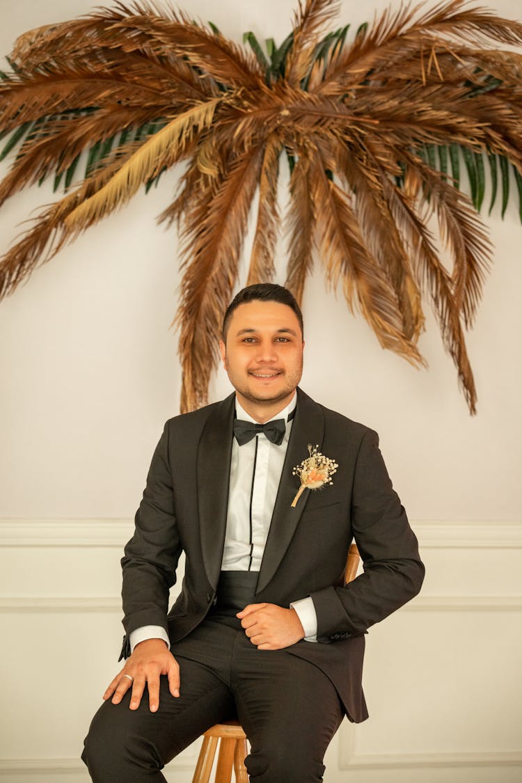 A Man In A Black Suit Sitting While Smiling