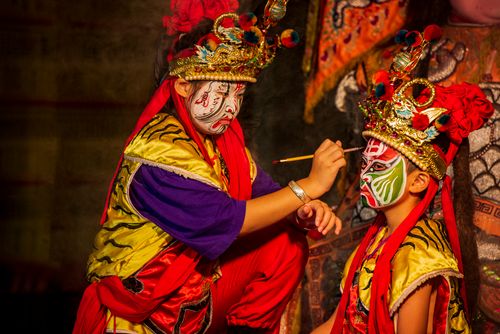 Free Two children applying vibrant traditional stage makeup in a cultural setting. Stock Photo