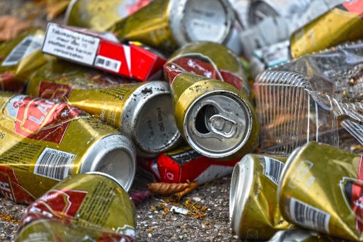 Pile of crushed beer cans and cigarette packs littering the pavement outdoors, suggesting pollution.