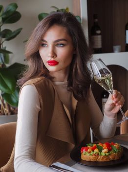Stylish woman sitting indoors, holding a champagne glass with vibrant red lips and sophisticated attire.