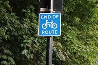 Close-up of an 'End of Route' bicycle sign amidst green leaves in London park.