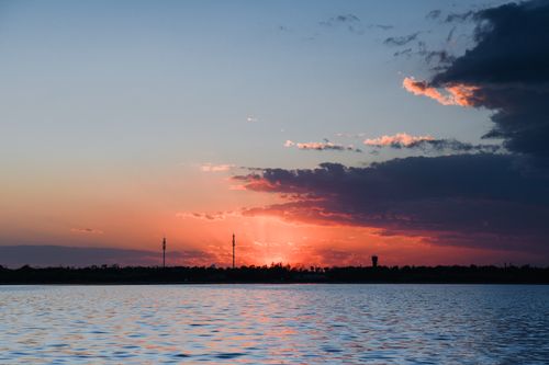 Free Serene sunset view over a lake with vivid sky hues and silhouette of distant landscape. Stock Photo
