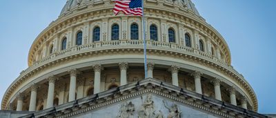 A detailed close-up of the United States Capitol dome and pediment with the American flag flying prominently.