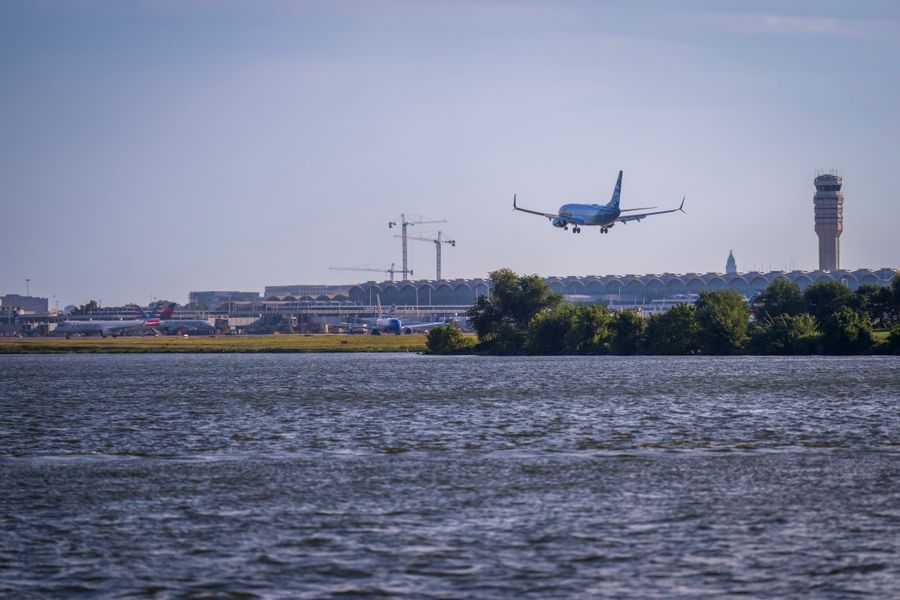 Blue airplane landing at BWI Airport with Washington DC skyline and control tower visible across the water