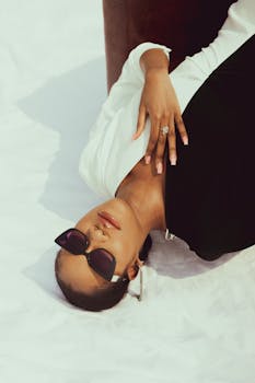 Stylish woman in sunglasses posing on a white background, showcasing elegant fashion.