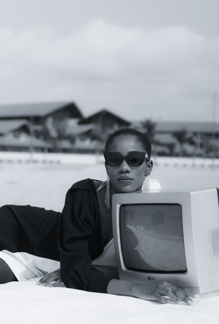 Stylish woman in sunglasses posing outdoors with a vintage TV set.
