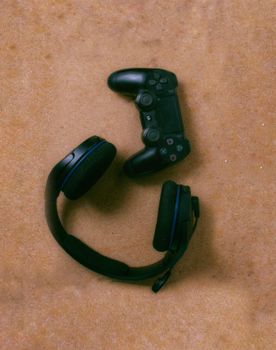 Top view of a game controller and headphones on a textured brown surface.