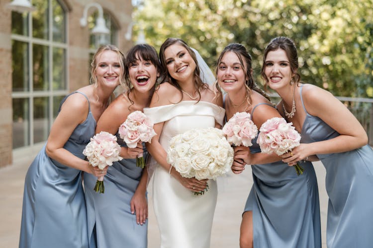 Woman In Wedding Dress With Her Bridesmaids Holding Bouquet Of Flowers