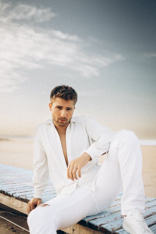 A Man in White Clothes Sitting on a Wooden Surface