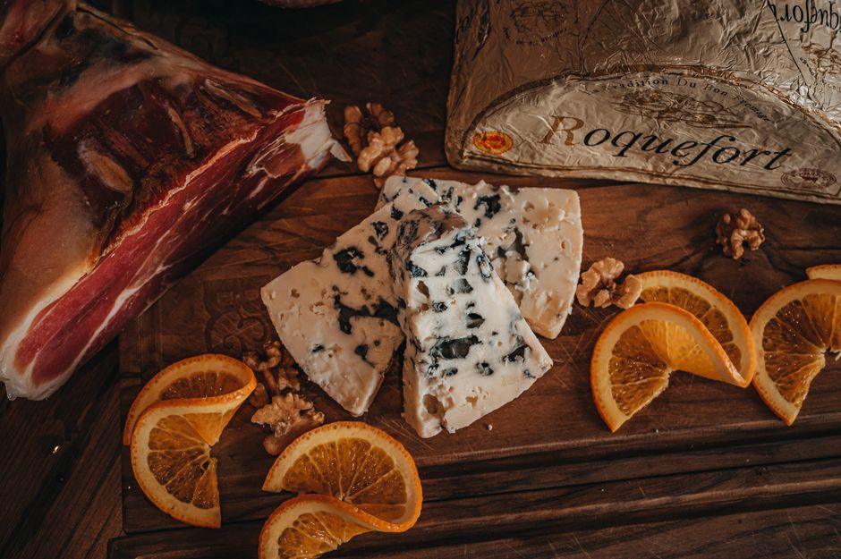 A wedge of Roquefort cheese cut open to show its ivory interior marbled with blue-green veins, resting on a wooden board with a knife.