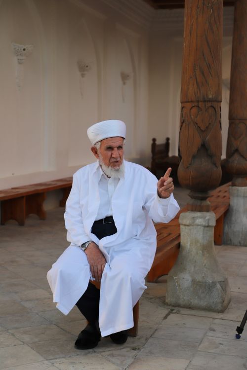 Free Elderly man in traditional Muslim clothing, seated outdoors, gesturing with his hand. Stock Photo