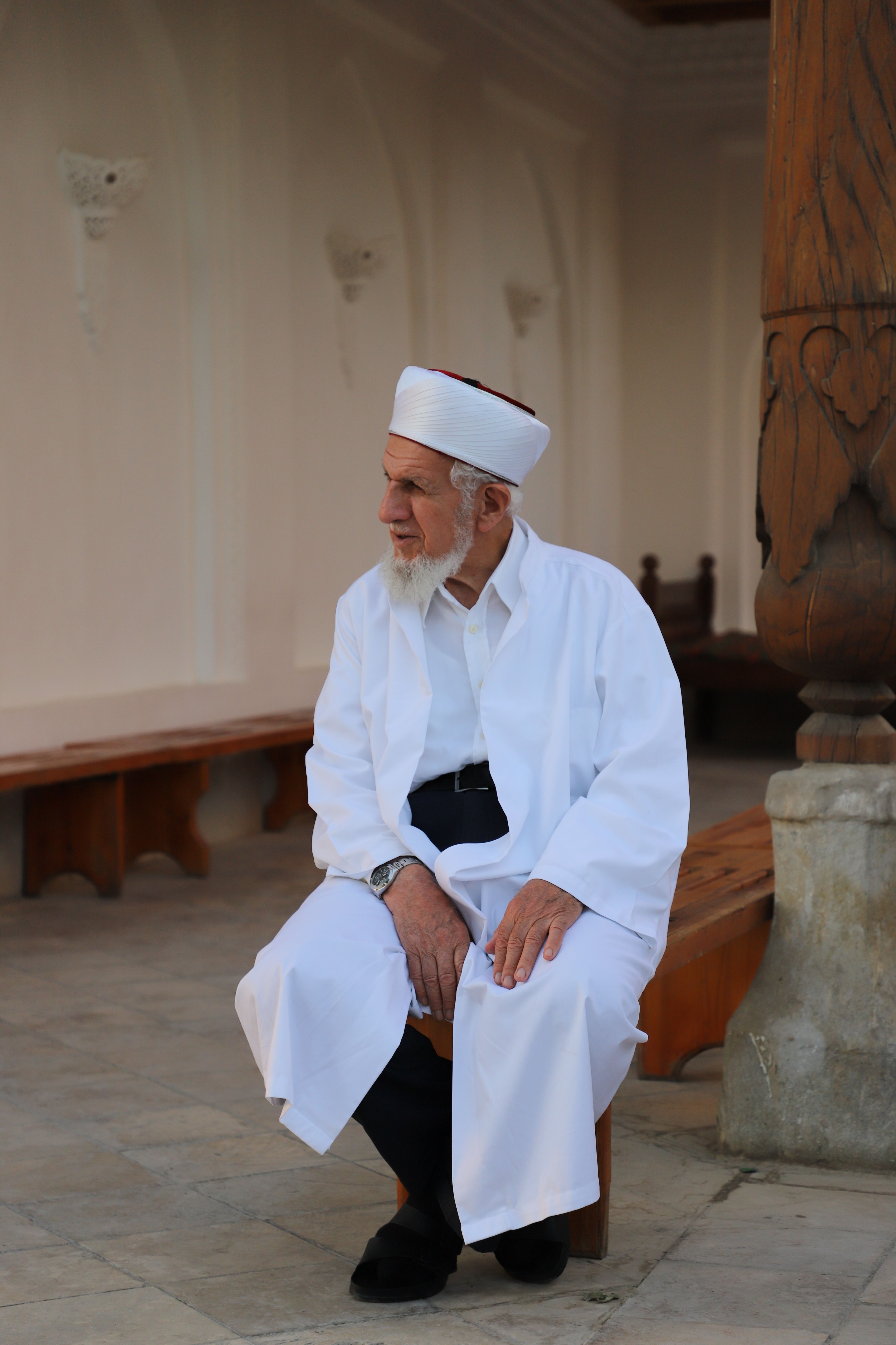 Elderly man in traditional white attire sitting indoors, captured in a peaceful moment.