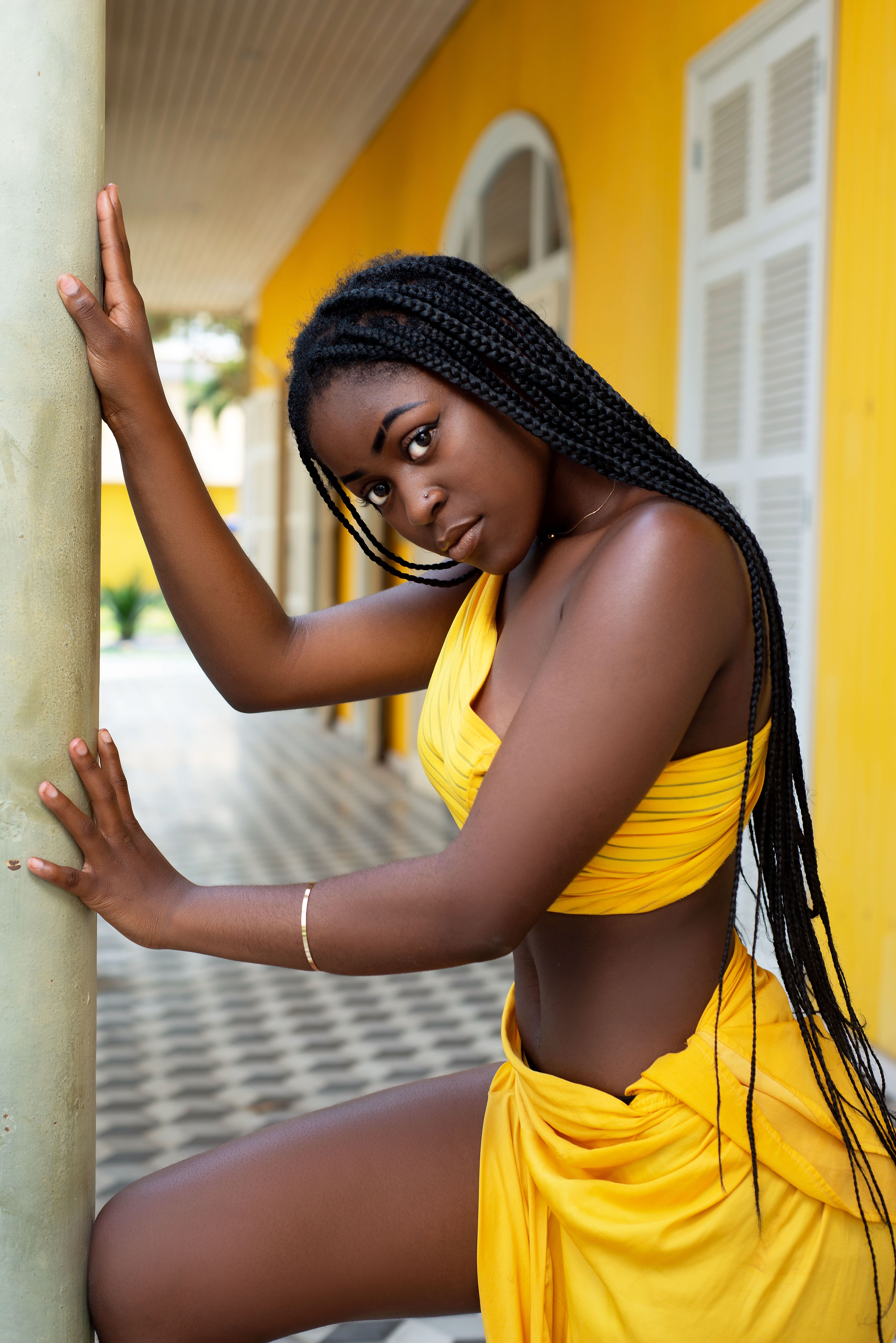 Chic fashion portrait of a young woman in a vibrant yellow outfit, showcasing modern style against a striking yellow wall.