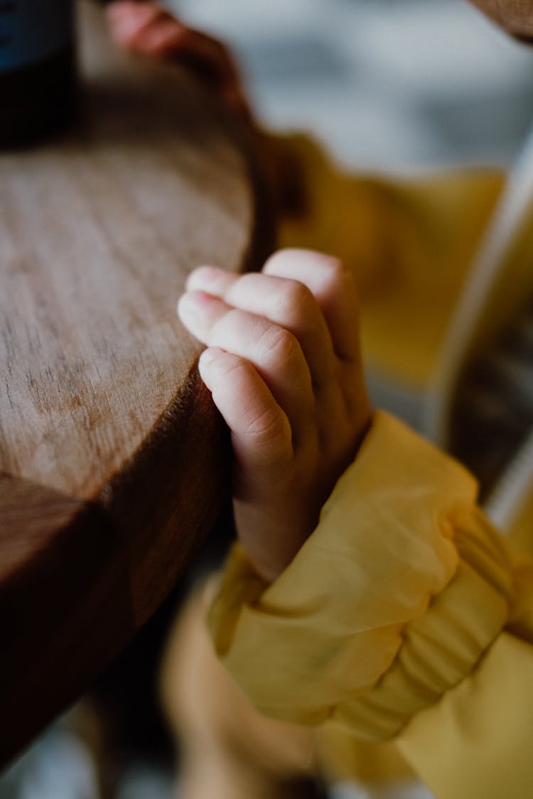 Close-up Of A Little Child Hand Holding The Edge Of The Table 