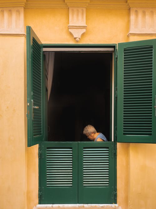 Free An elderly woman sits by an open green shuttered window in Otranto, Italy. Stock Photo
