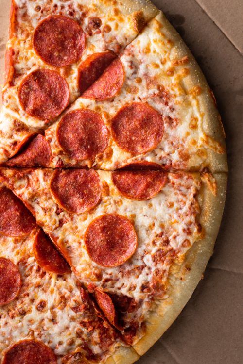 Free Close-up of a hot pepperoni pizza sliced vertically on a cardboard background. Stock Photo