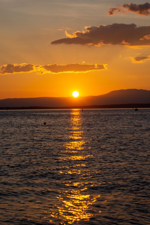 Free A breathtaking ocean sunset with golden reflections on the water and silhouetted mountains. Stock Photo