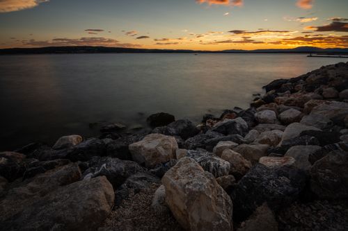 Free Tranquil sunset view over a rocky shore with calm ocean waters and vivid skyline. Stock Photo