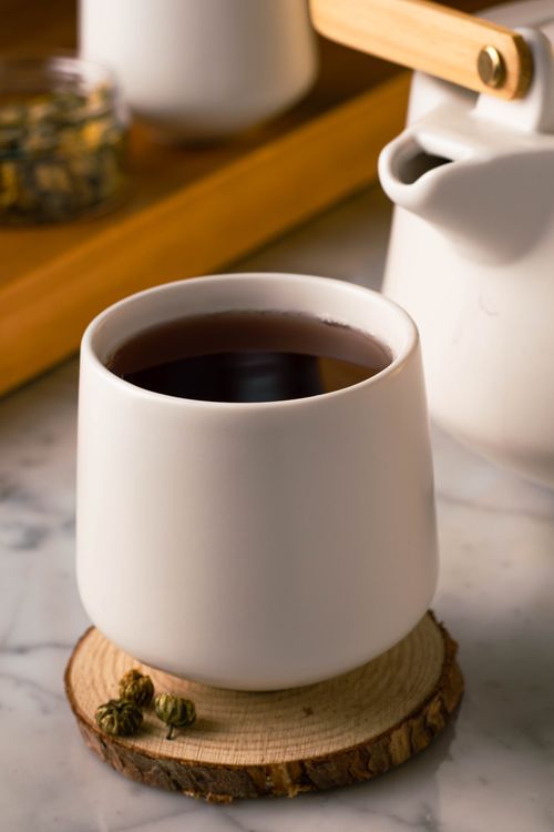 Free Close-up of a ceramic tea cup with herbal tea on a wooden coaster, indoor setting. Stock Photo