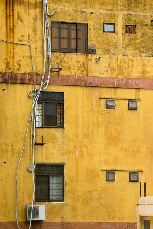 Free Close-up of a worn yellow building facade with windows and cables in Ho Chi Minh City. Stock Photo
