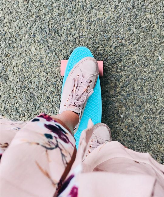 Close-up of a person skateboarding with pink sneakers and a floral dress on a blue skateboard.