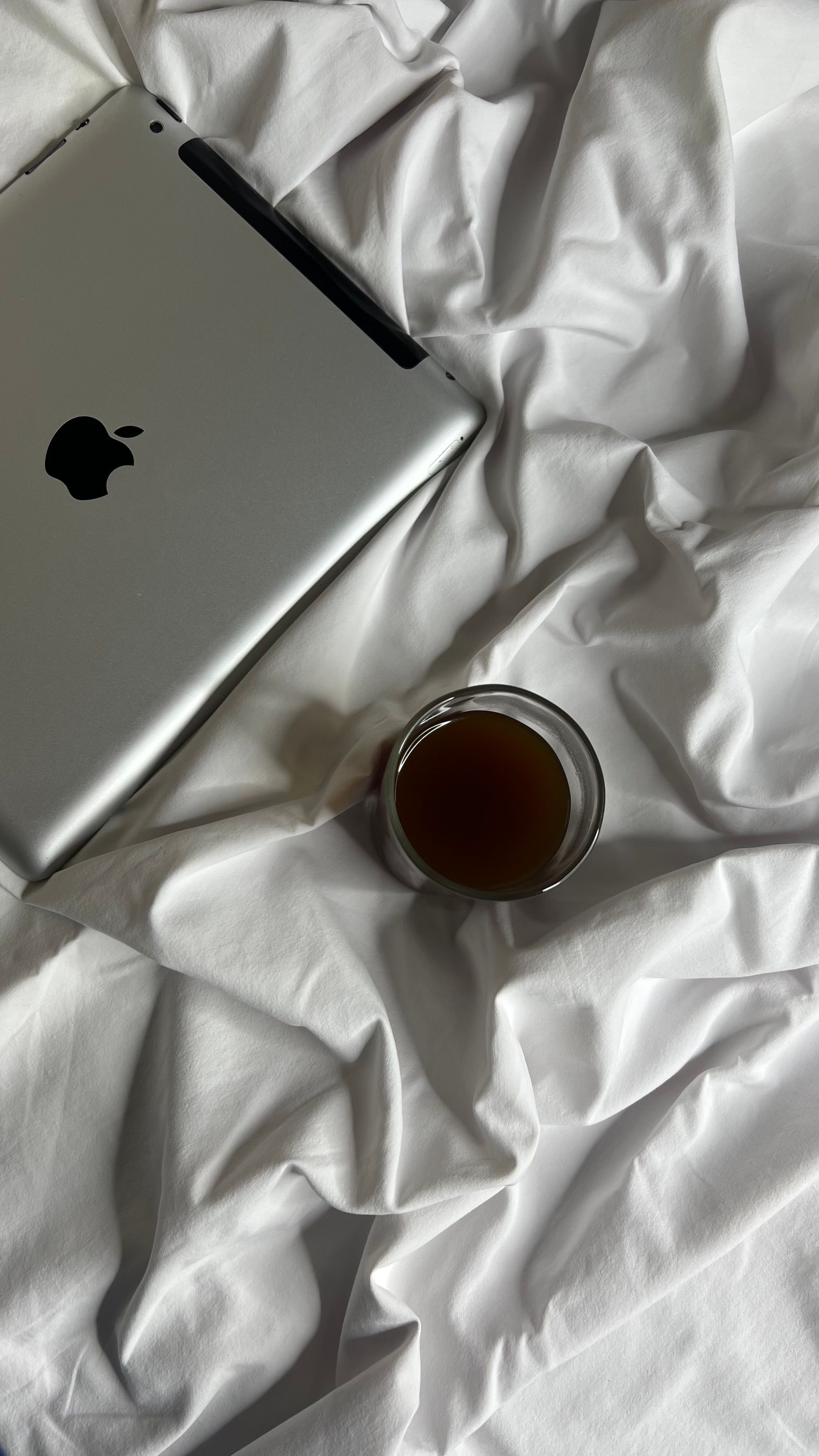 Top view of a tablet and coffee cup on a crumpled white bed textile for a cozy morning vibe.