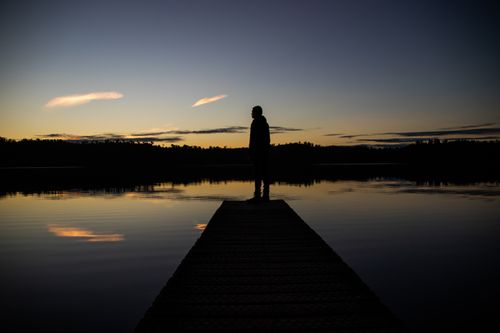Free A serene silhouette of a person standing on a dock during sunset, capturing the tranquil reflections in the water. Stock Photo