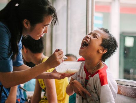 Joyful moment as a woman feeds a happy child in a warm, indoor setting.