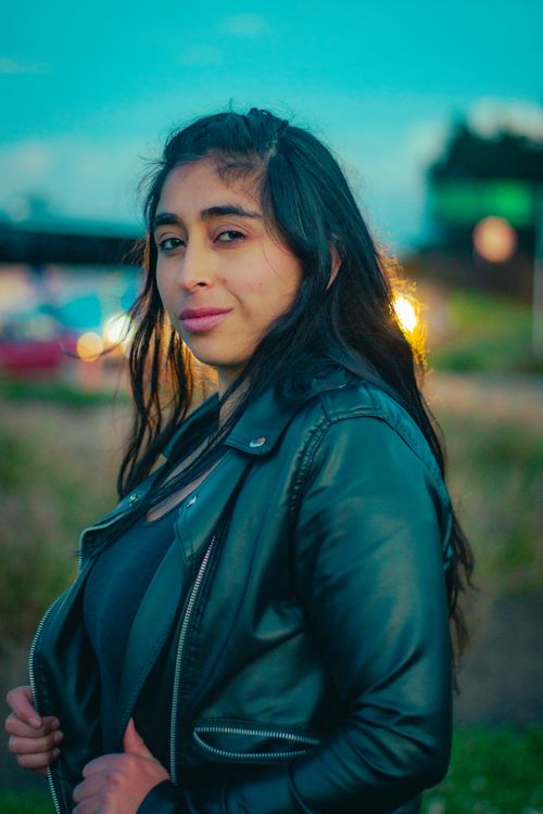Free Stylish woman in black leather jacket posing outdoors with blurred city lights. Stock Photo
