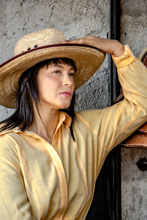 Free Stylish woman in a straw hat and yellow shirt posing outdoors in vibrant light. Stock Photo