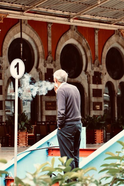 Free Senior man smoking near architectural arches, captured from behind. Stock Photo