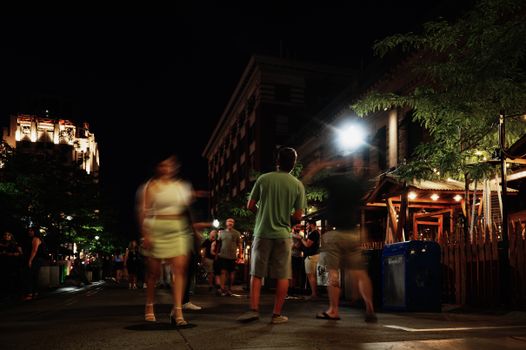 A lively street at night with people walking, capturing motion blur and urban nightlife atmosphere.